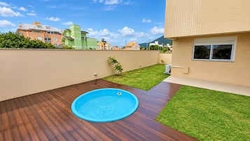 A swimming pool on a wooden deck with a small grassy area and a wall.