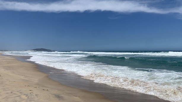 Una playa con olas, cielo despejado y una isla distante.