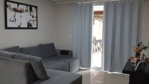 Una sala de estar con un sofá gris, un televisor de pantalla plana y una ventana con cortinas claras.