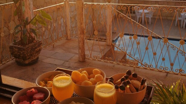 Un balcón con una mesa dispuesta para el desayuno, con vista a una piscina y un paisaje rural al atardecer.