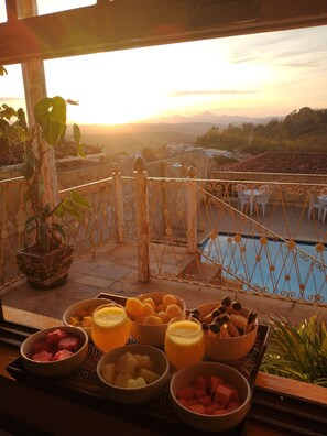 A balcony with a table set for breakfast, overlooking a pool and a scenic view of the countryside during sunset. - HOTEL MONTANHAS DE MINAS  (Diamantina)