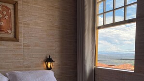 Habitación de hotel con una cama grande, una lámpara de noche, una ventana con vistas al paisaje y un cuadro en la pared.