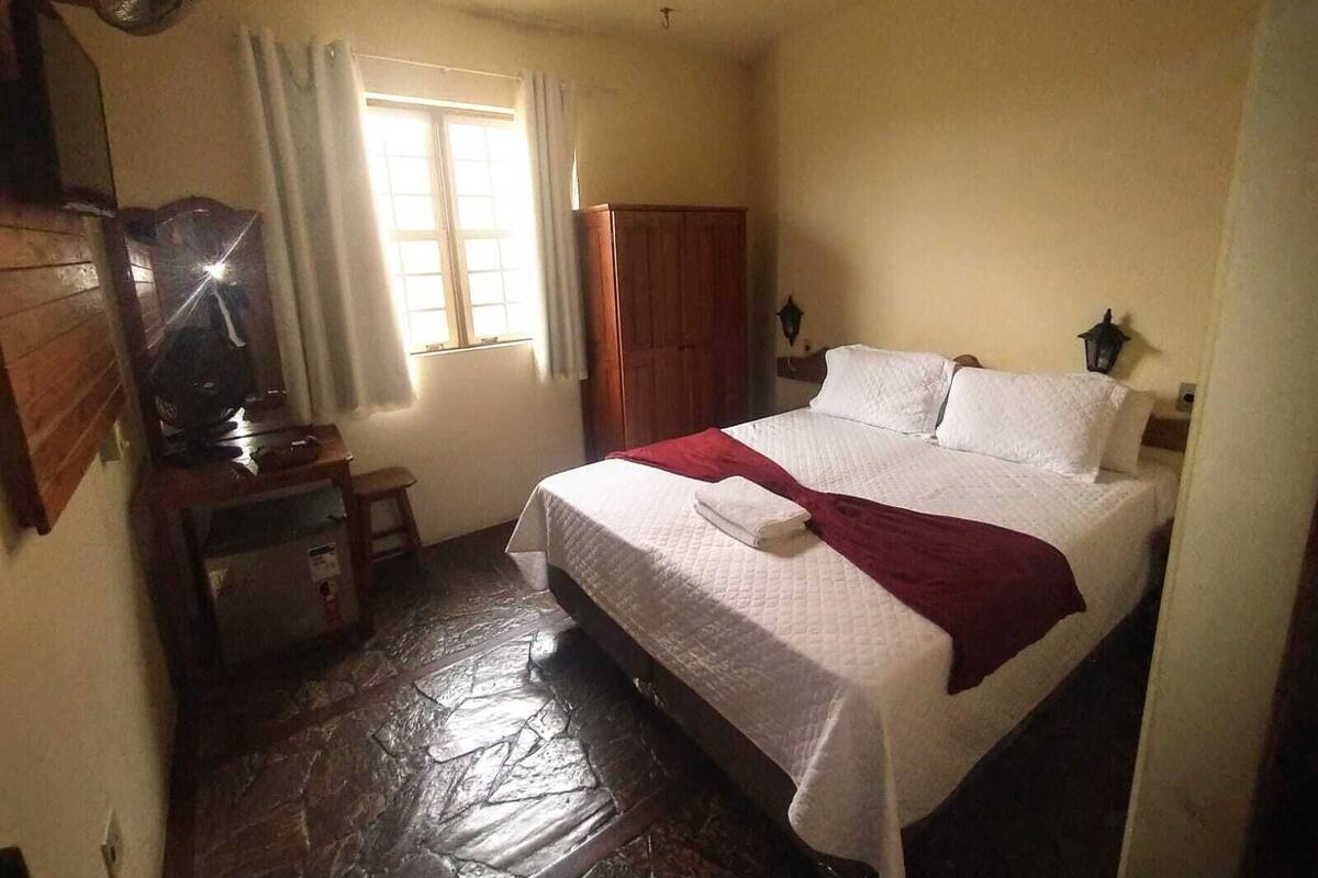 A bedroom with a bed, a desk, a chair, a window with curtains, and a wardrobe.