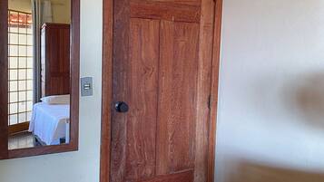 Una puerta de madera con un espejo en la pared, una cama con cubrecama blanco y un pequeño taburete de madera.