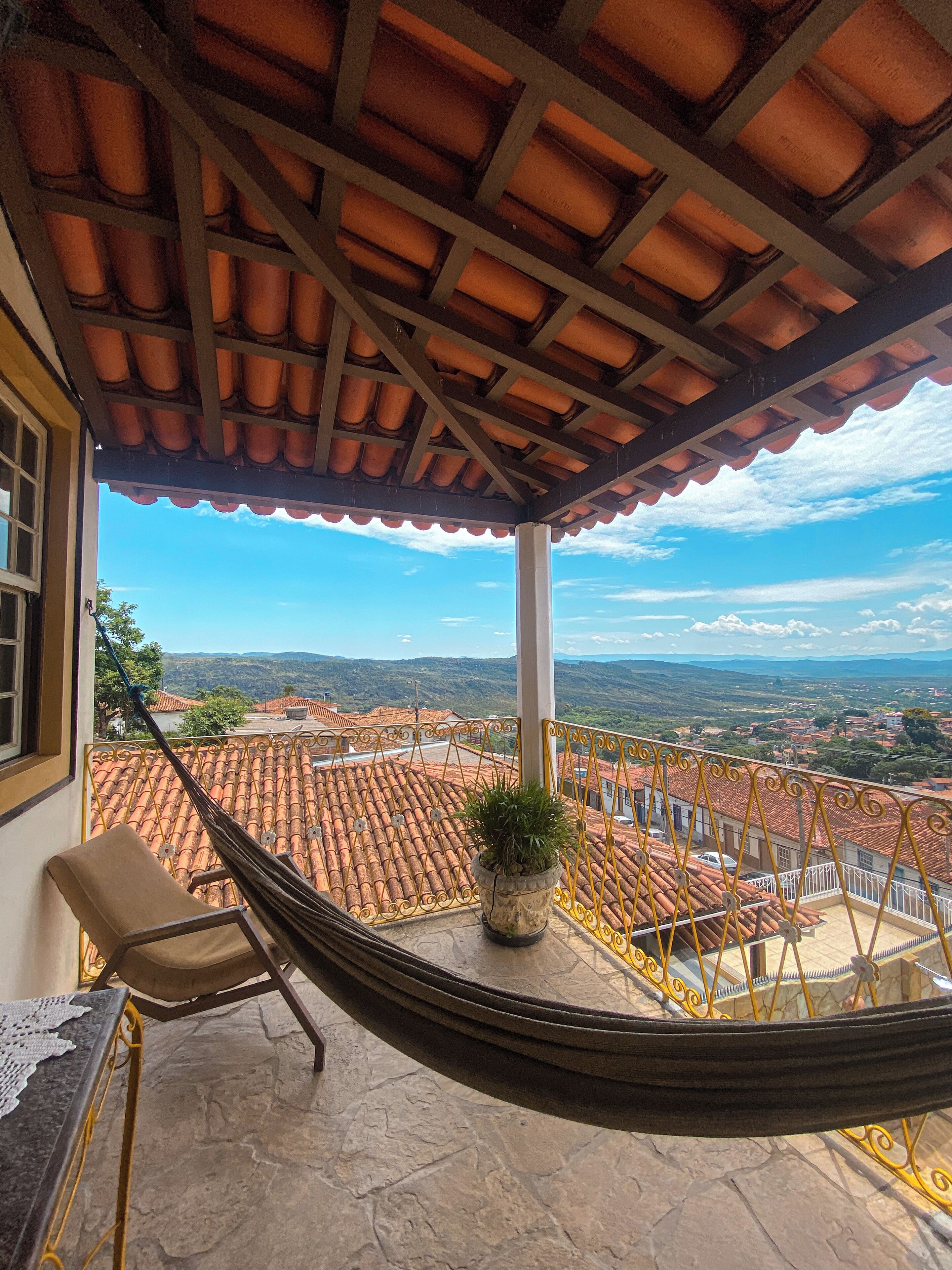 A hammock on a balcony with a view of terracotta-roofed buildings and a clear sky.