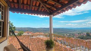 A hammock on a balcony with a view of terracotta-roofed buildings and a clear sky.