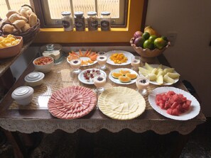 A table with various food items and condiments, including plates of sliced fruits, a bowl of bread, and jars of spices. - HOTEL MONTANHAS DE MINAS  (Diamantina)