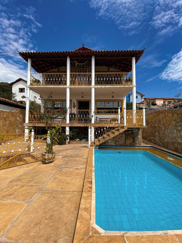 A two-story building with a balcony, a swimming pool, and a stone wall. - HOTEL MONTANHAS DE MINAS  (Diamantina)