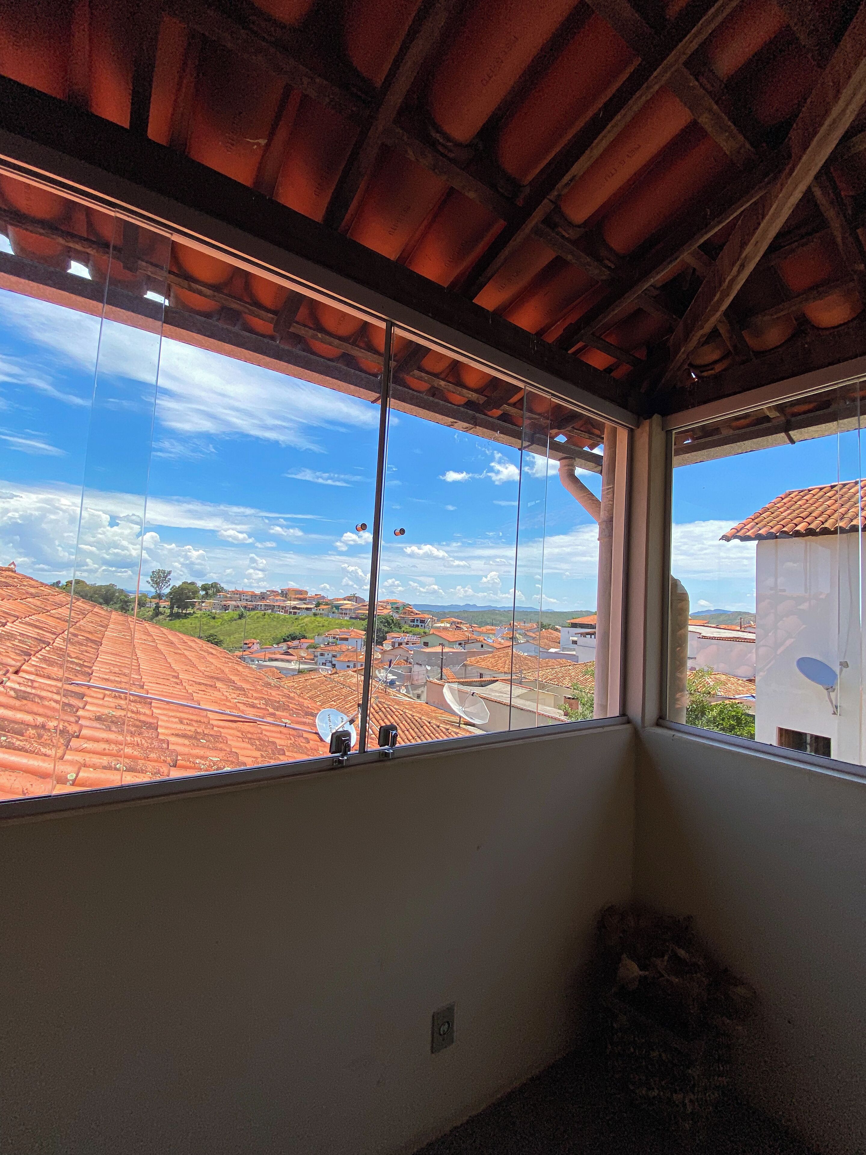 A room with a large window overlooking a town with red-tiled roofs and a clear blue sky.