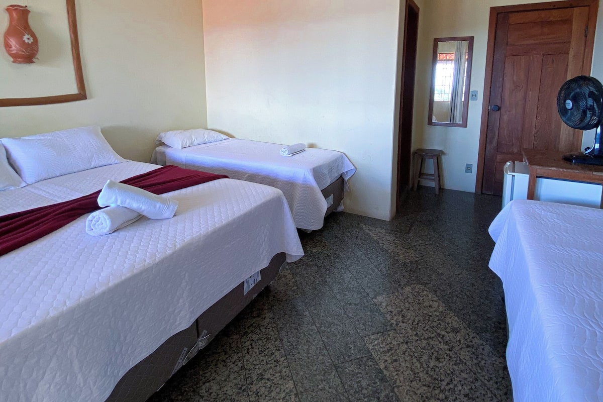 A hotel room with two beds, a wooden door, a fan, and a small stool.