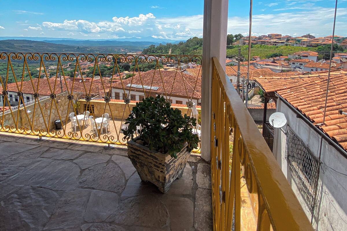 A balcony with a stone floor, a potted plant, and a view of a town with red-roofed buildings.