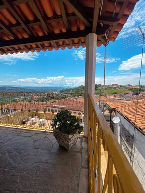A balcony with a stone floor, a potted plant, and a view of a town with red-roofed buildings. - HOTEL MONTANHAS DE MINAS  (Diamantina)