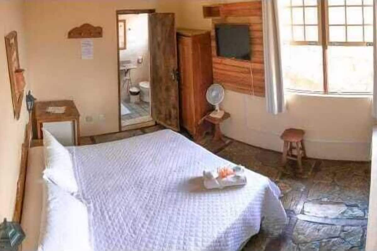 A room with a bed, a wooden cabinet, a mirror, and a window.