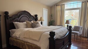 A bedroom with a large bed, a chair, a lamp, and a window with curtains. - Great house in Inglewood, walking distance to Zoo, Downtown, Restaurants  (Calgary)
