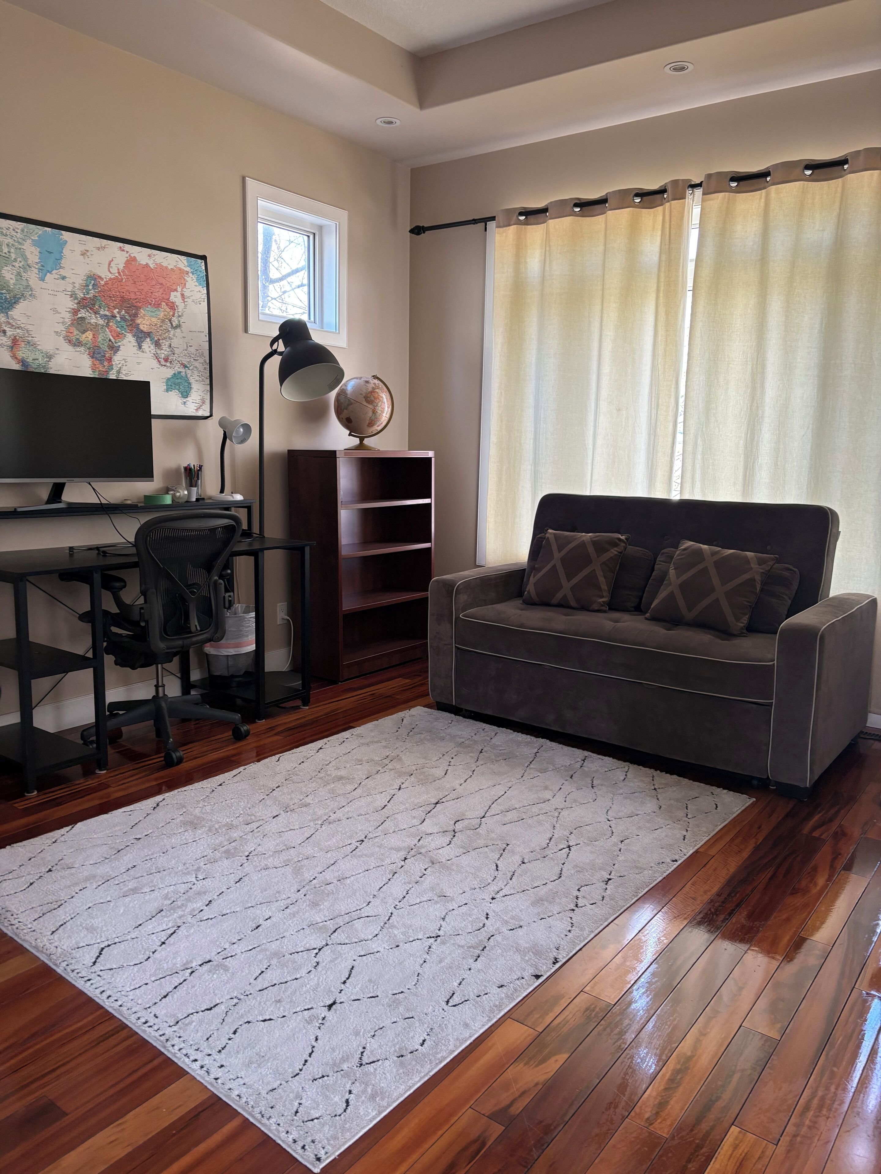 A living room with a desk, computer, chair, sofa, globe, and a world map on the wall.