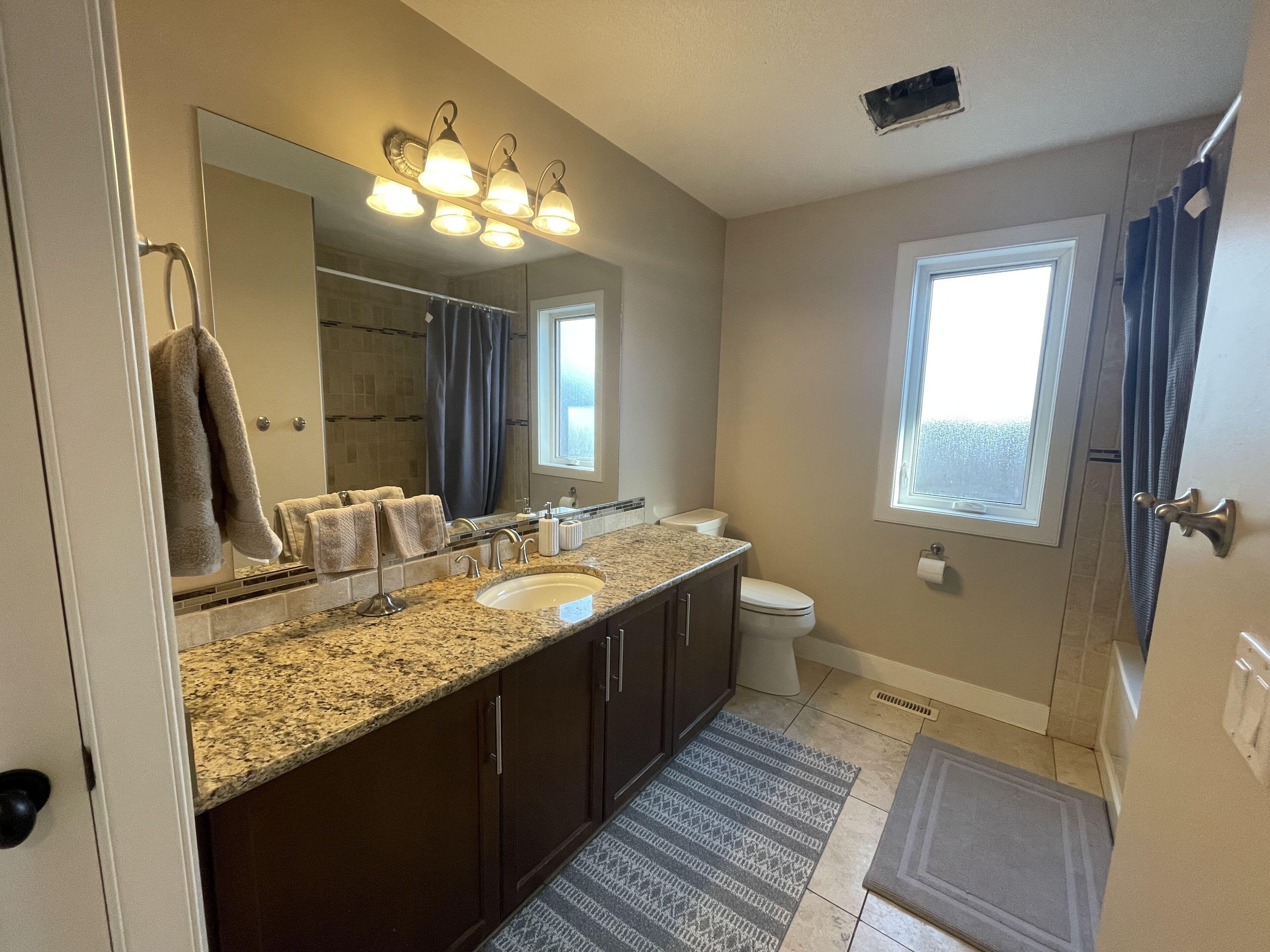 A bathroom with a granite countertop sink, a large mirror, a toilet, and a shower area.
