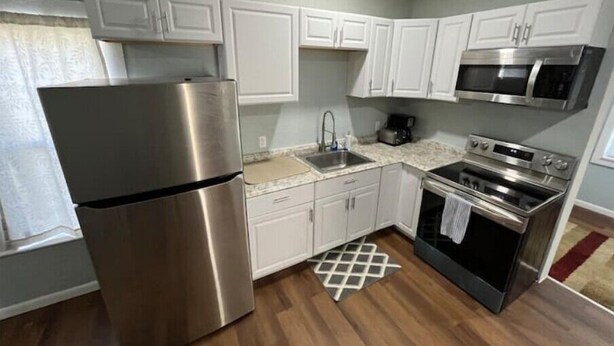 A compact kitchen with white cabinets, a stainless steel refrigerator, a microwave, and a stove. - The Fort Pierce 

 (Fort Pierce)
