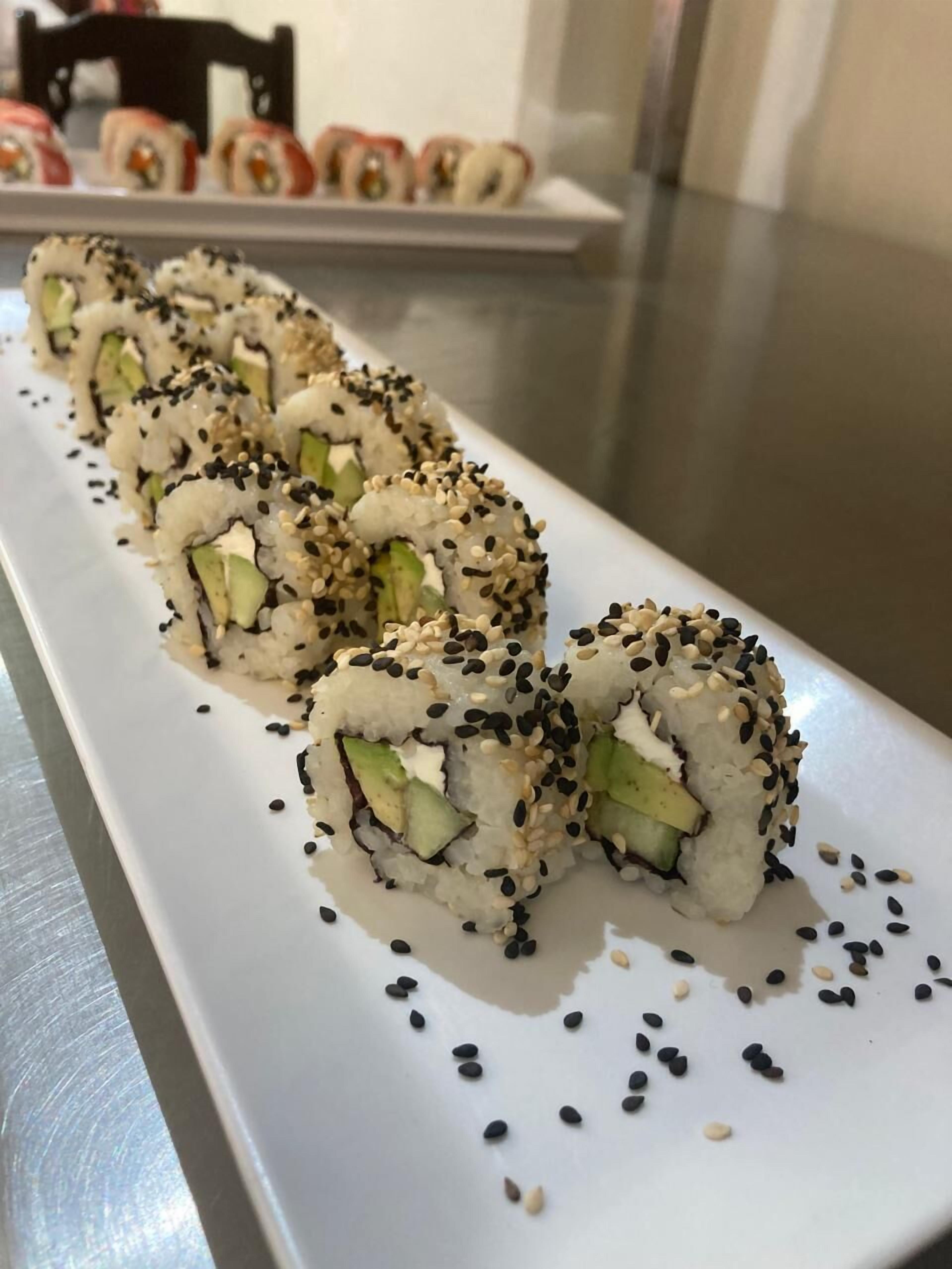 A white rectangular plate with sushi rolls topped with sesame seeds, arranged in a row.
