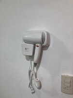 A white hair dryer mounted on a wall with a power outlet nearby.