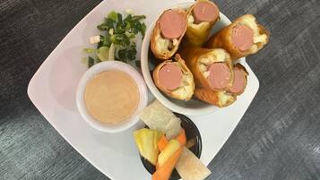 A plate with sausage rolls, a small bowl of sauce, and some vegetables.