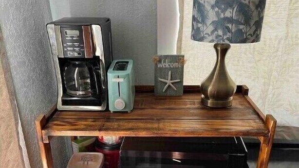 Een houten plank met een koffiezetapparaat, een broodrooster, een welkomstbord en een lamp.