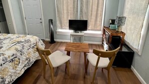 Een kamer met een bed, een televisie op een standaard, een klein tafeltje met stoelen, een raam met gordijnen en een deur.