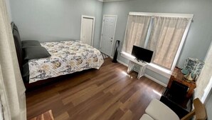 Een slaapkamer met een bed, een televisie op een meubel, een raam met gordijnen en een deur.