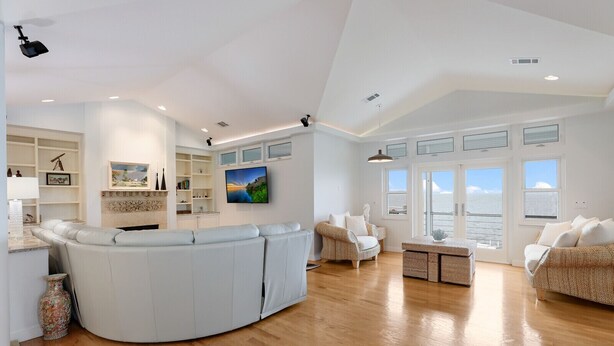 Een ruime woonkamer met een gebogen witte bank, een eettafel en uitzicht op de zee door grote ramen.