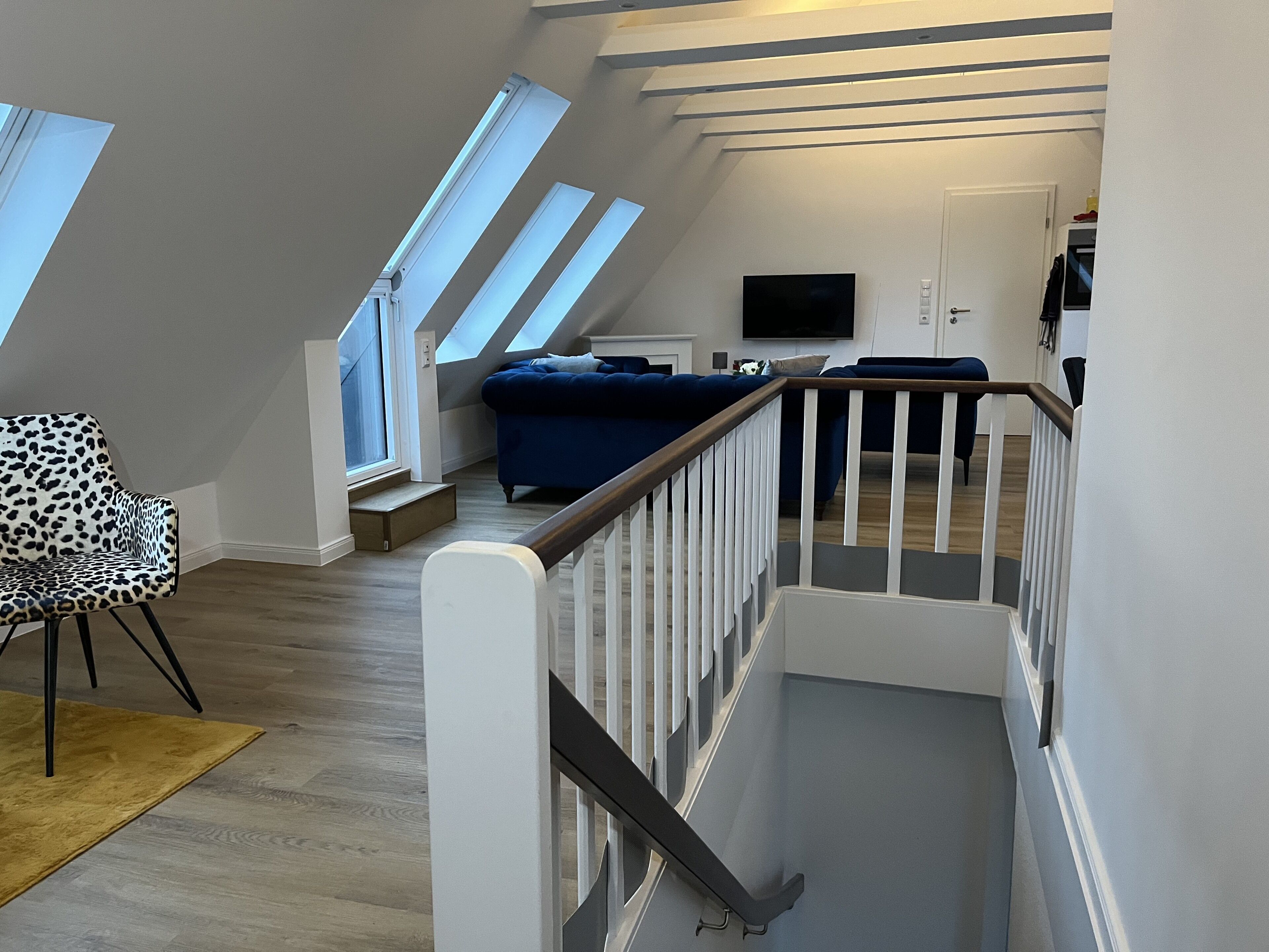 A modern loft bedroom with skylights, a staircase, a leopard print chair, and a blue sofa.