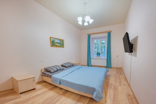 A bedroom with a bed, a nightstand, a painting, a window with curtains, and a TV mounted on the wall. - H&B apartments Zubalashvili (Tbilisi)