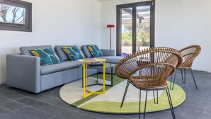 Un salon moderne avec un canapé gris, des coussins colorés, une table basse jaune et des fauteuils en osier.