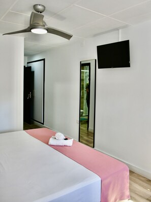 A hotel room with a bed, a ceiling fan, a TV, and a mirror. - Hostal Garden Rous (Paiporta)