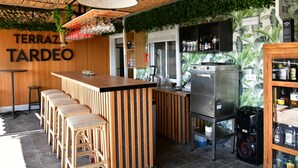 Een bar met een houten toonbank, barstoelen en een koelkast.