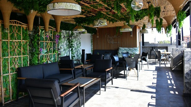 Een terras met zwarte banken, houten tafels en hangplanten.