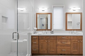 Ein modernes Badezimmer mit Duschkabine aus Glas, Waschtisch aus Holz mit mehreren Schubladen und zwei Wandspiegeln.