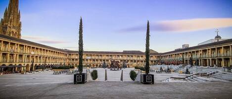 A spacious courtyard with a central fountain, surrounded by a classical building with a tall spire.