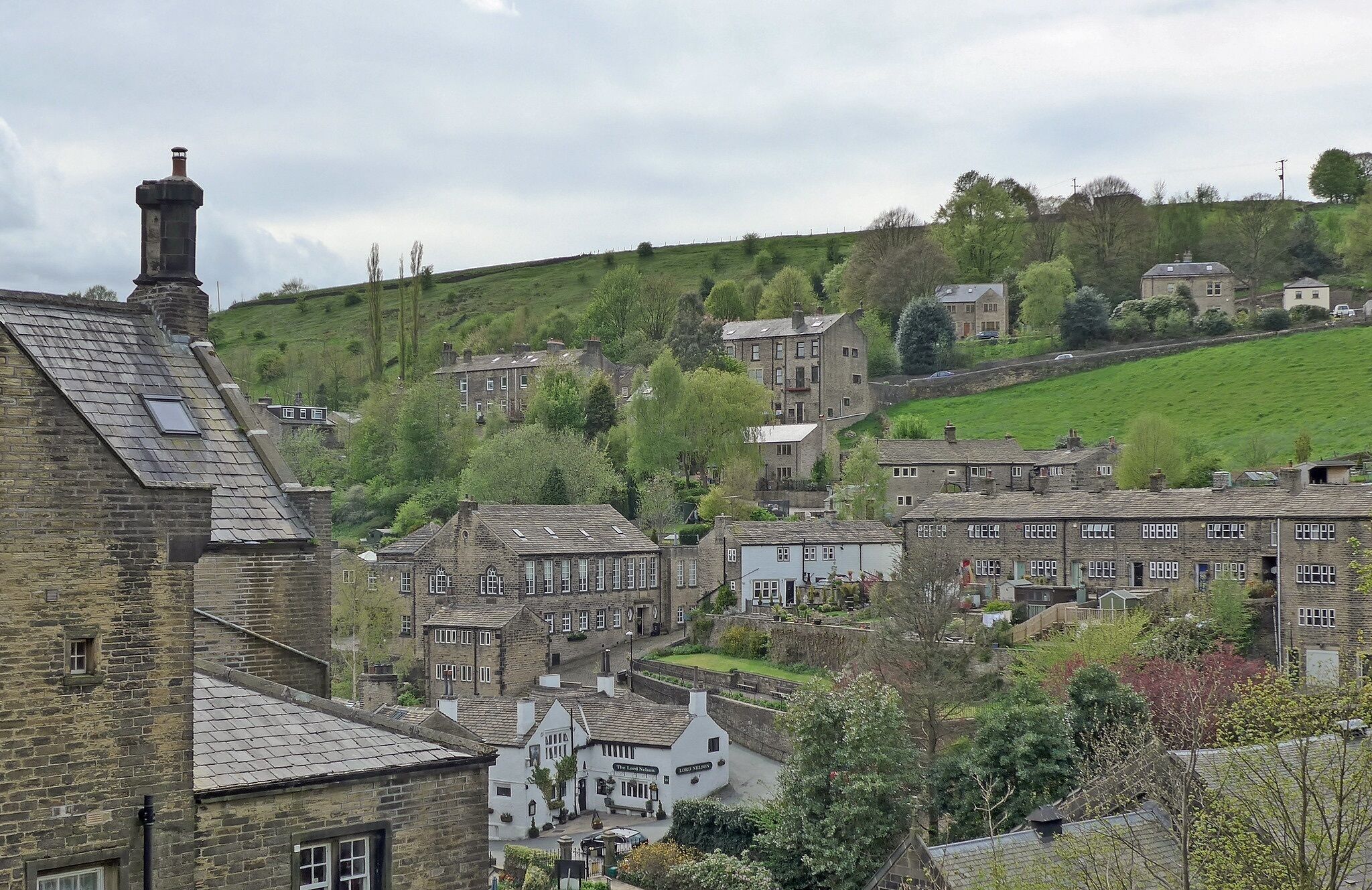 A traditional stone building with a steeply pitched roof, likely a pub or inn, surrounded by a small village with similar architecture.