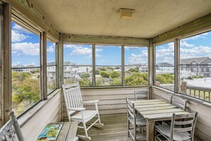 Un porche cubierto con mobiliario de madera, ventanas amplias y vistas de edificios circundantes.