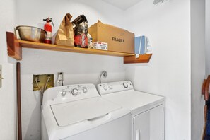A laundry area with a white washer and dryer, a shelf with various items including a box labeled 'FRAGILE,' and a fire extinguisher.