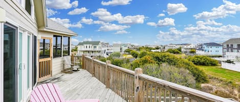 A wooden deck with a pink Adirondack chair, overlooking a residential area with houses and a clear sky.