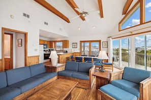 Amplia sala de estar con muebles de madera, una cocina al fondo y ventanas grandes con vistas a la ciudad.