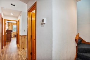 A hallway with wooden flooring, a wooden door, and a white textured wall with a thermostat.