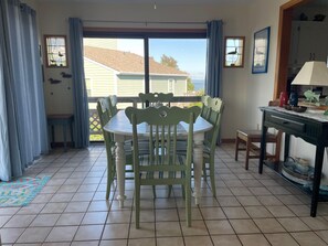 Un coin repas avec une table et des chaises, une vue à travers une porte vitrée et un meuble contenant des objets décoratifs.