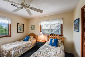 Une chambre avec deux lits, un ventilateur de plafond et deux fenêtres avec des rideaux.