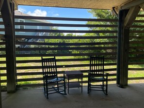 A covered patio area with two chairs and a small table, overlooking a grassy yard and a house.