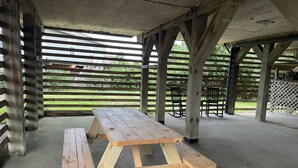 Ein Picknicktisch mit Bänken unter einer Holzpergola mit Blick auf eine Rasenfläche.