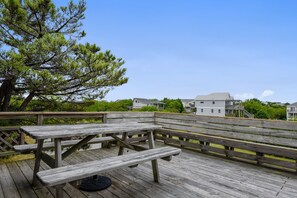 Una terraza de madera con mesas de picnic y bancos, con vista a una zona residencial con casas y árboles.