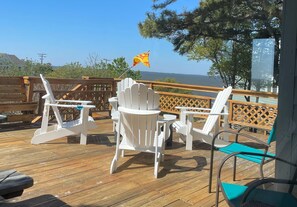 Eine Holzterrasse mit weißen Adirondack-Stühlen und einem Tisch, mit Blick auf ein Gewässer.