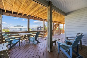 Una terrazza esterna in legno con tavoli e sedie da picnic, una zona coperta con soffitto in legno e vista su case sullo sfondo.