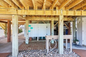 A wooden structure with a covered area, a white door, and a small table with a hose. - Carolina Hideaway -- Kitty Hawk Home just steps to the beach with Elevator (Kitty Hawk)